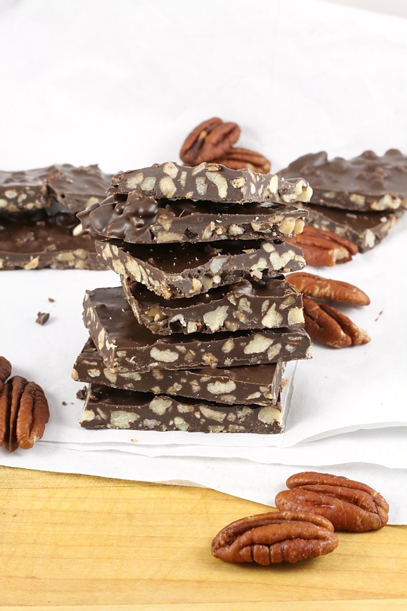 A stack of chocolate pecan bark stacked on a cutting board with parchment paper.