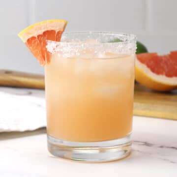Lowball glass filled with pink grapefruit margarita with a salted rim.