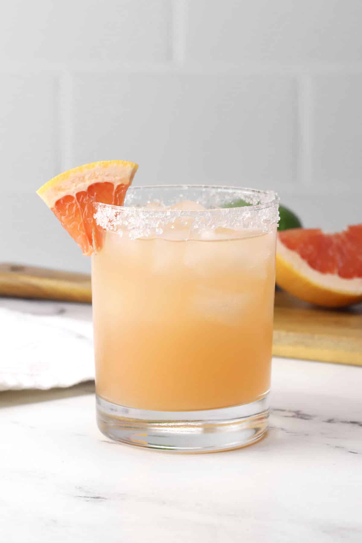 Lowball glass filled with pink grapefruit margarita with a salted rim.
