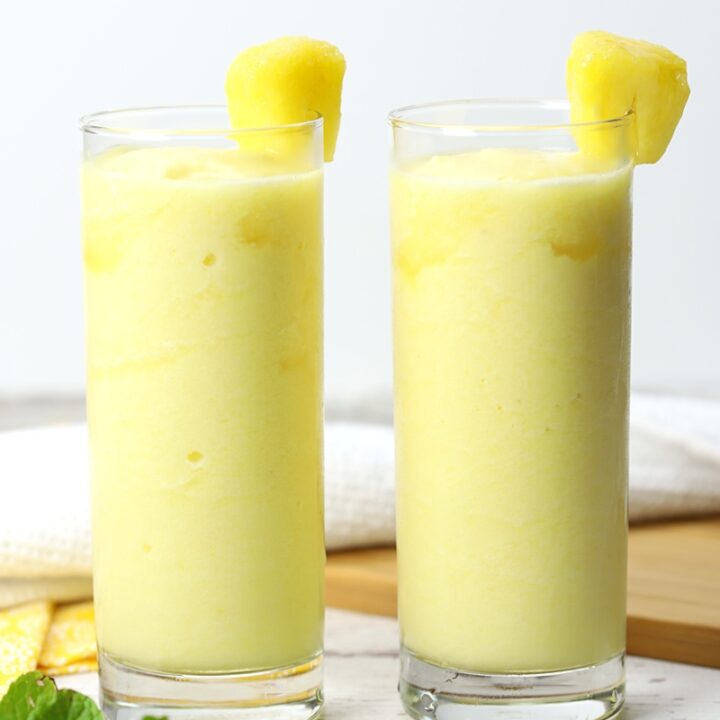 Two glasses of pineapple rum slush on a white counter top.