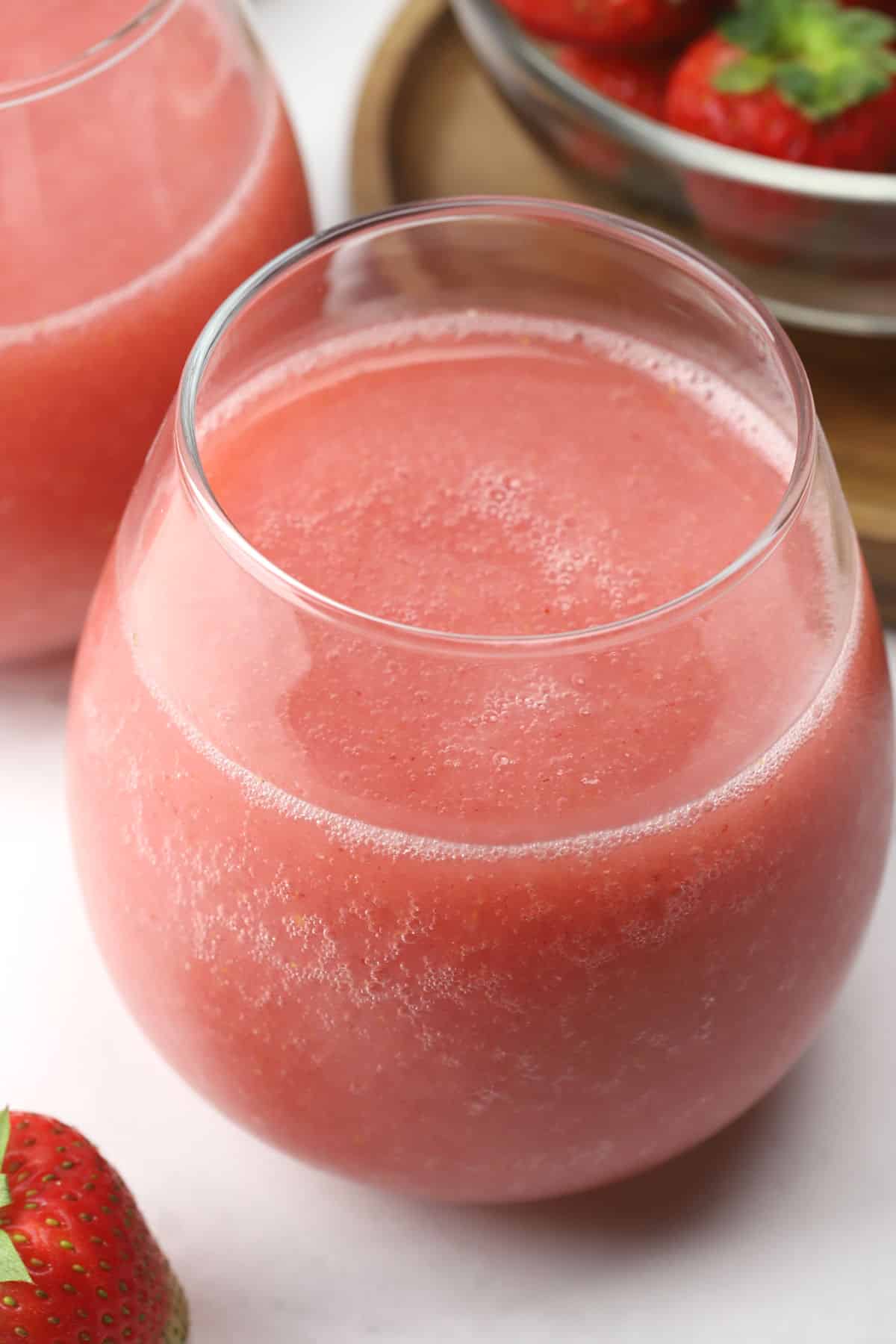 Close up of a stemless wine glass filled with pink slushy frosé .