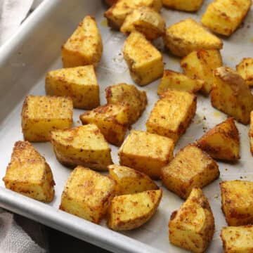 A metal sheet pan filled with oven roasted seasoned potatoes.