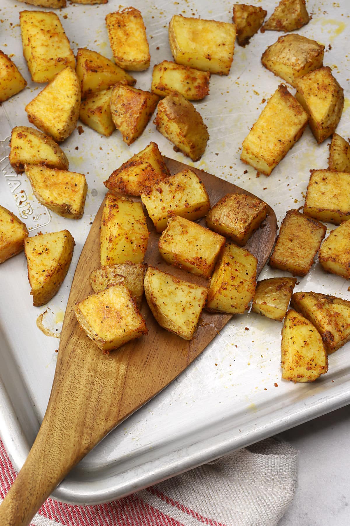 A wooden spatula scooping roasted potatoes from a sheet pan.