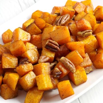 A white serving dish filled with cubed butternut squash and pecans.