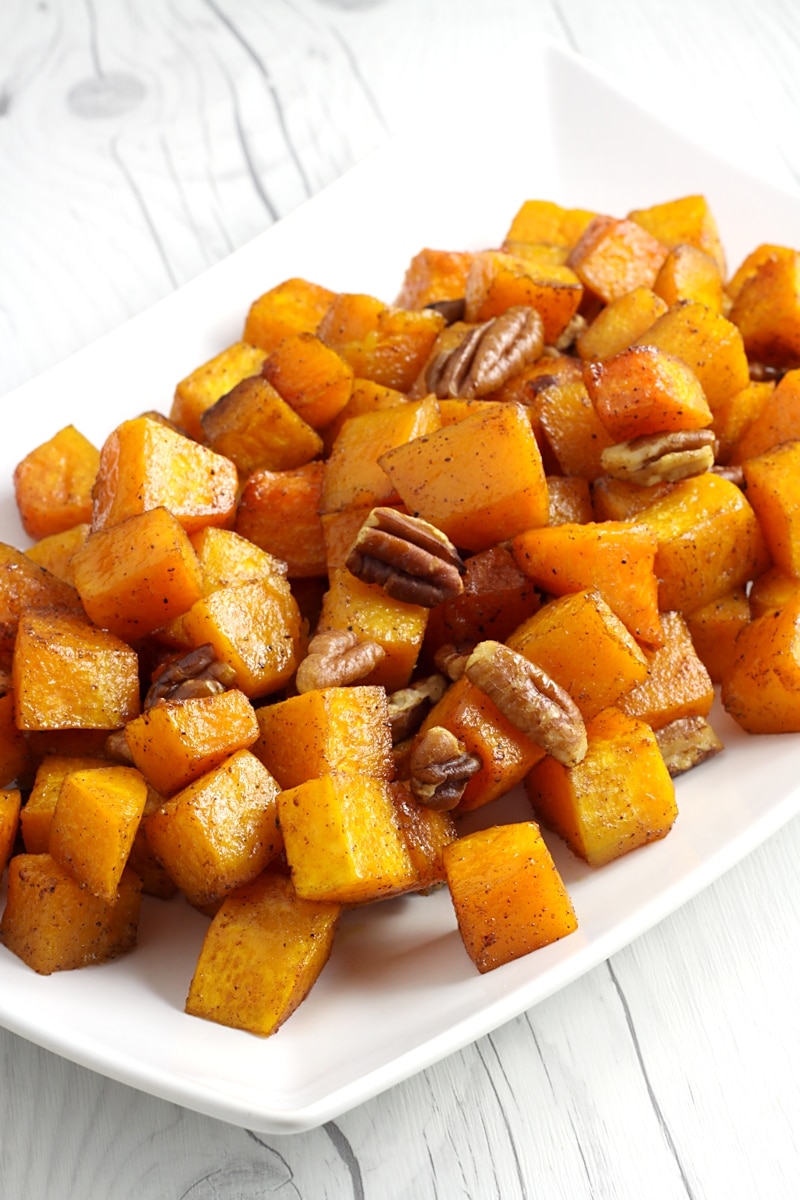 A white serving dish filled with cubed butternut squash and pecans.