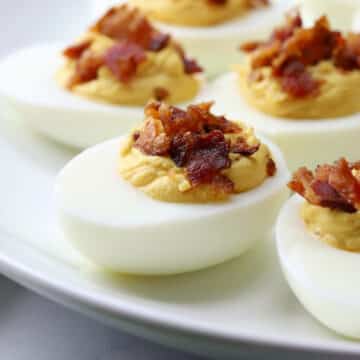 Deviled egg topped with crumbled bacon on a white plate.
