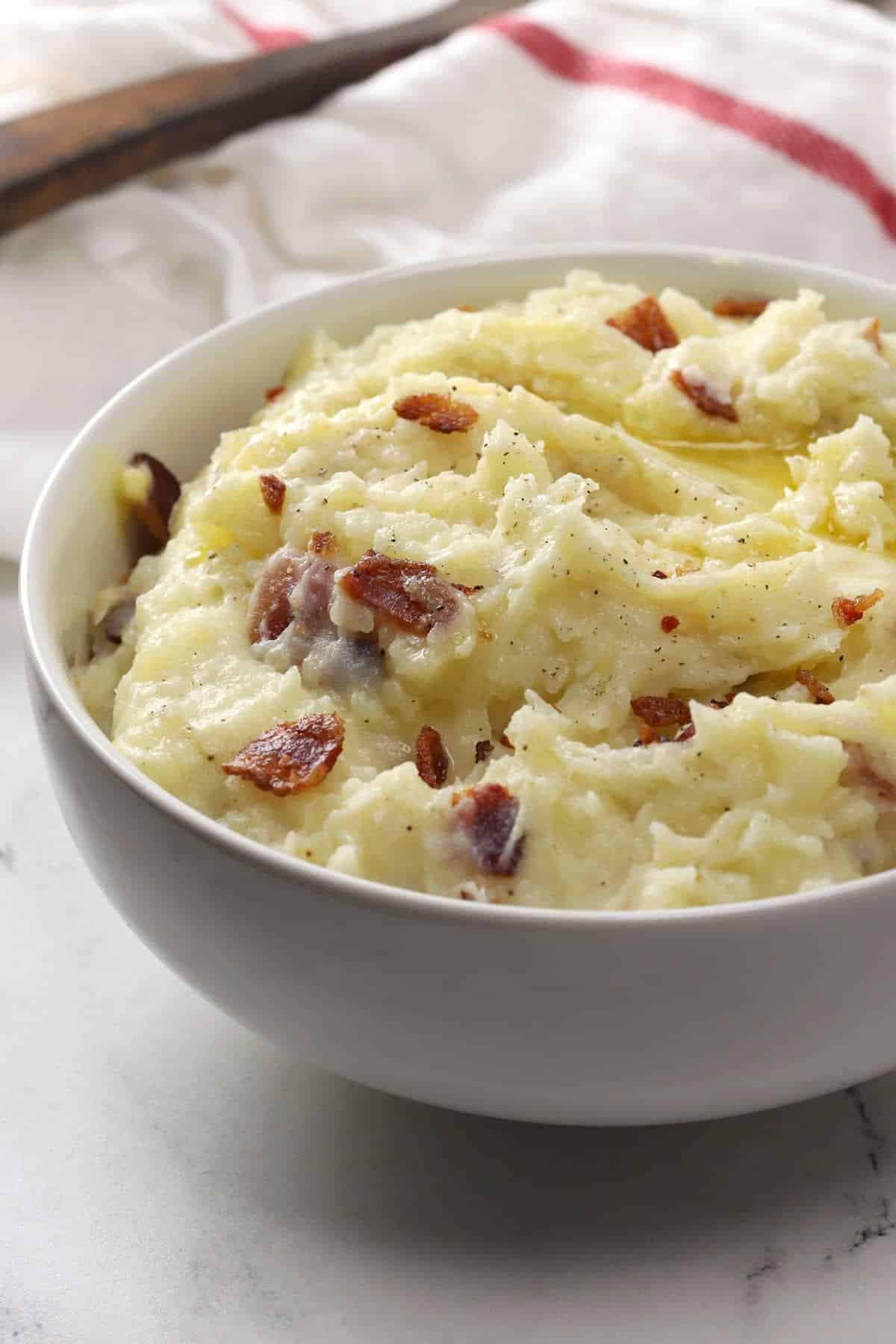 White bowl filled with mashed potatoes filled with small bacon pieces.
