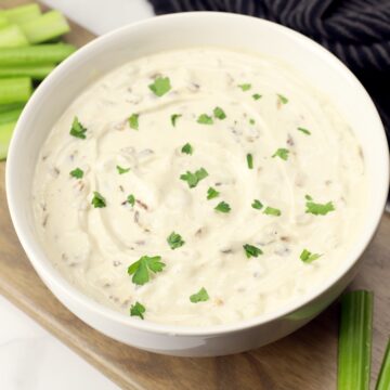 A white bowl filled with Greek yogurt French onion dip topped with chopped parsley.