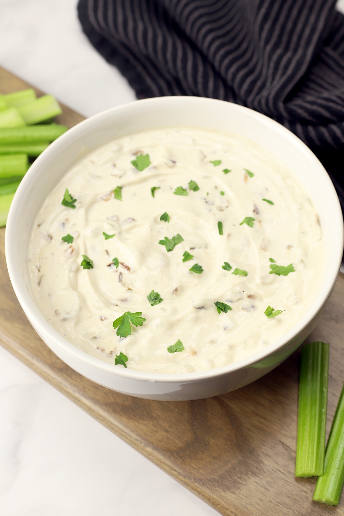 A white bowl filled with Greek yogurt French onion dip topped with chopped parsley.