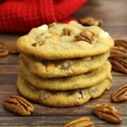 A stack of butter pecan cookies with pecans scattered on a counter top.
