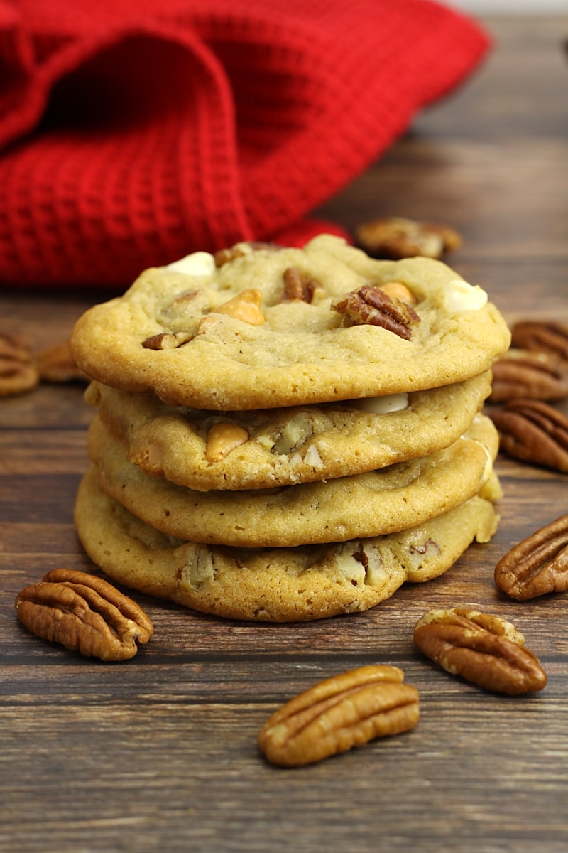 A stack of butter pecan cookies with pecans scattered on a counter top.