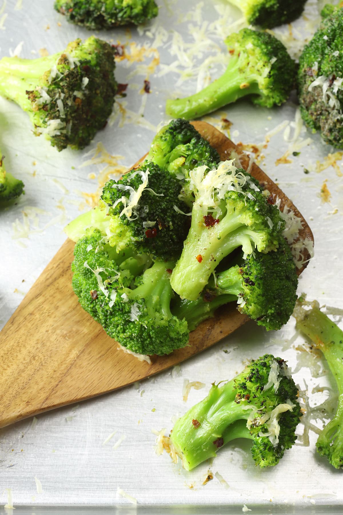 Wooden spatula filled with roasted broccoli on a metal sheet pan.