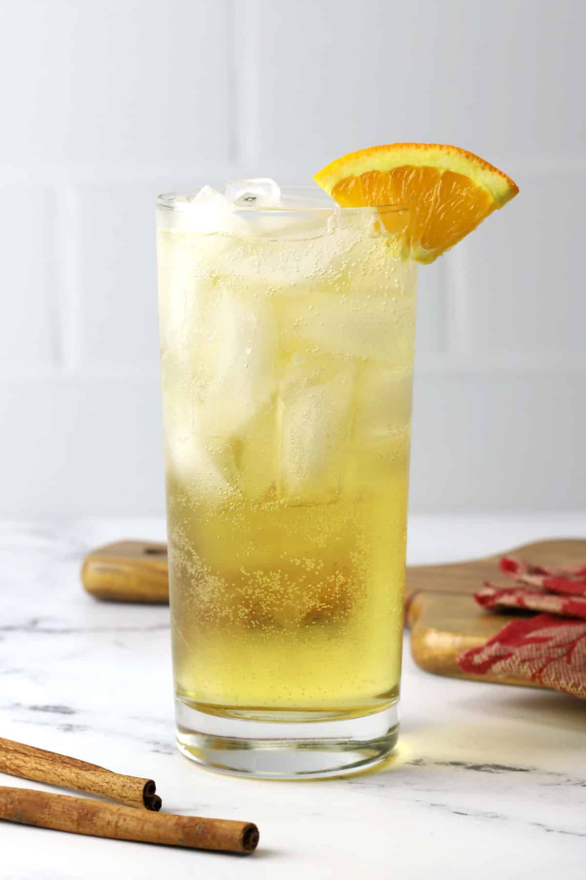 A glass of spiced orange ginger ale cocktail on a countertop, garnished with an orange slice.