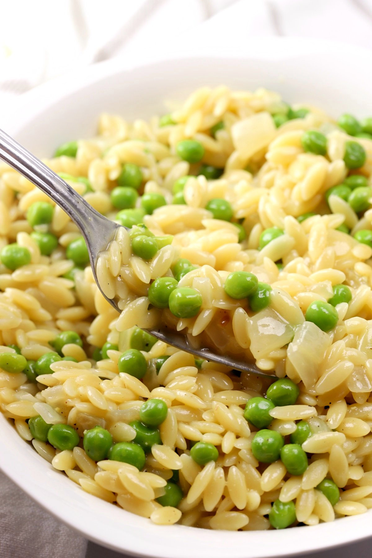 A metal fork filled with orzo and peas.