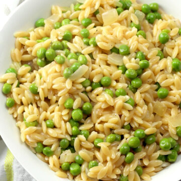 A white bowl filled with orzo and peas.