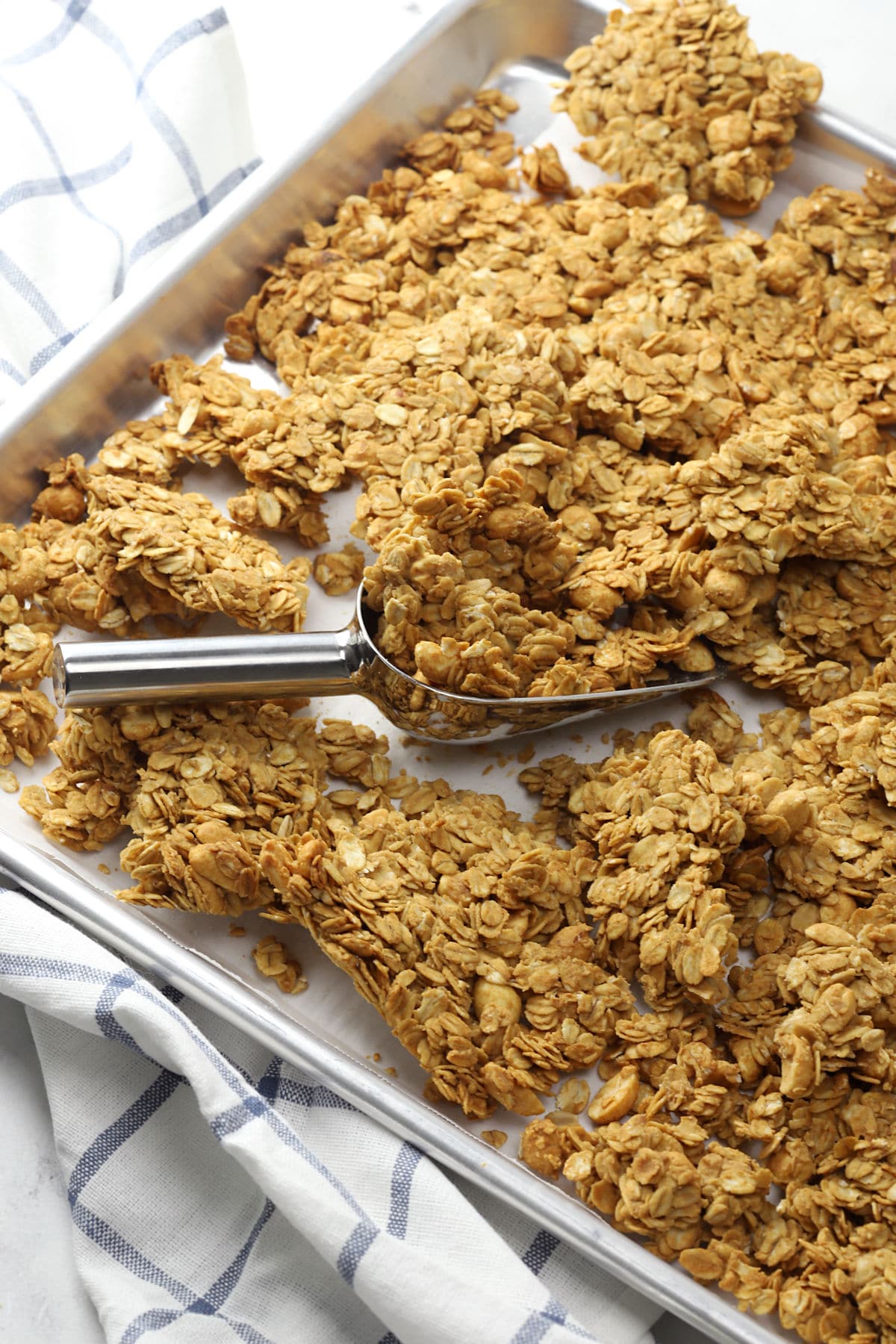 Metal sheet pan filled with peanut butter granola and a metal scoop.