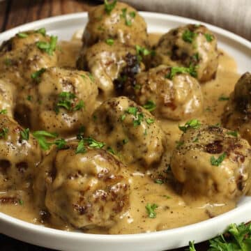 A round serving plate filled with Swedish meatballs covered in gravy and topped with a parsley garnish.