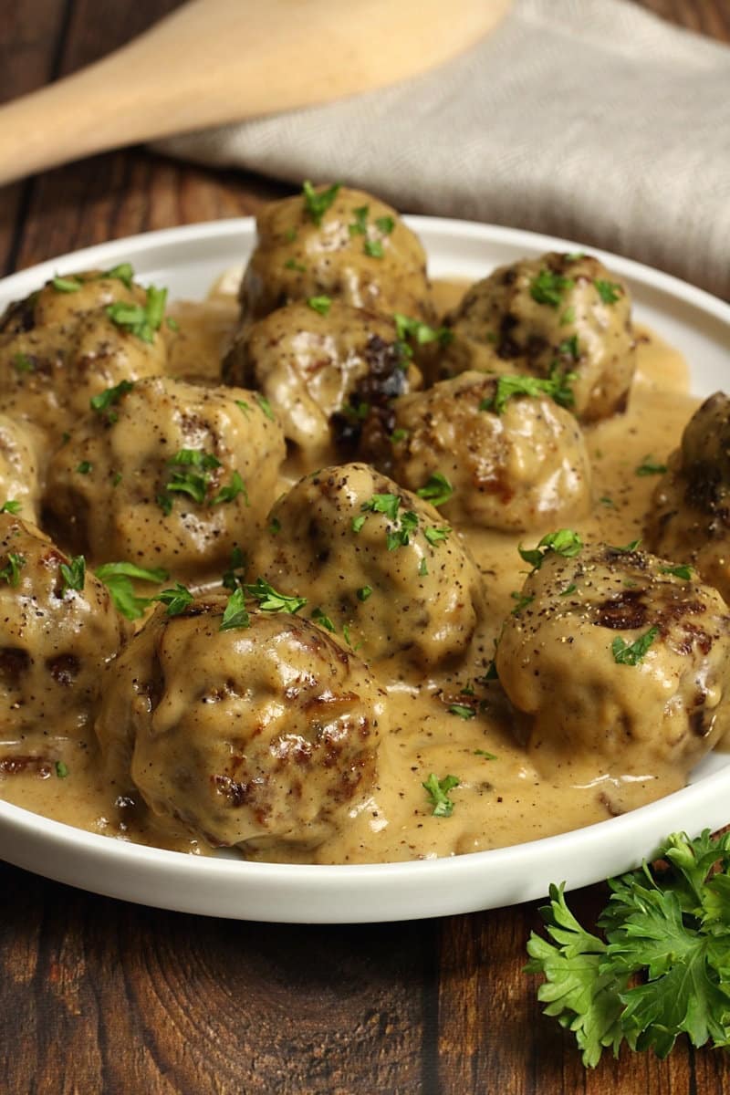 A round serving plate filled with Swedish meatballs covered in gravy and topped with a parsley garnish.