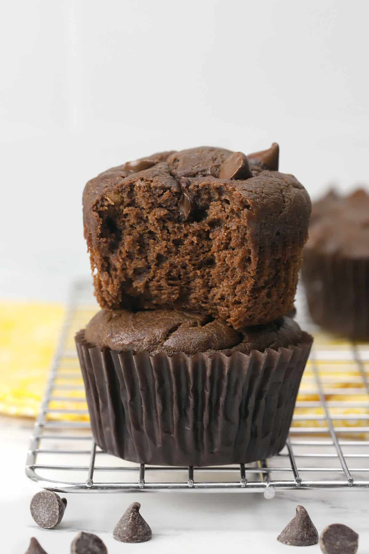 Two chocolate peanut butter banana muffins stacked, one with a bite missing.