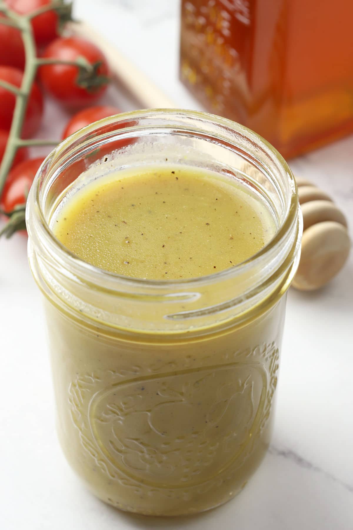 Jar of honey mustard dressing next to a jar of honey and cherry tomatoes.