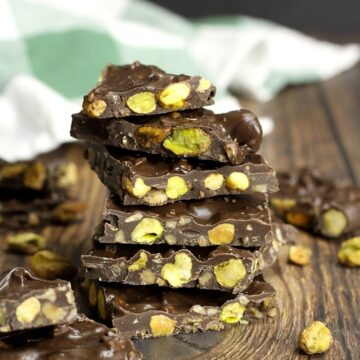 A stack of dark chocolate pistachio bark piece stacked on a wooden countertop.