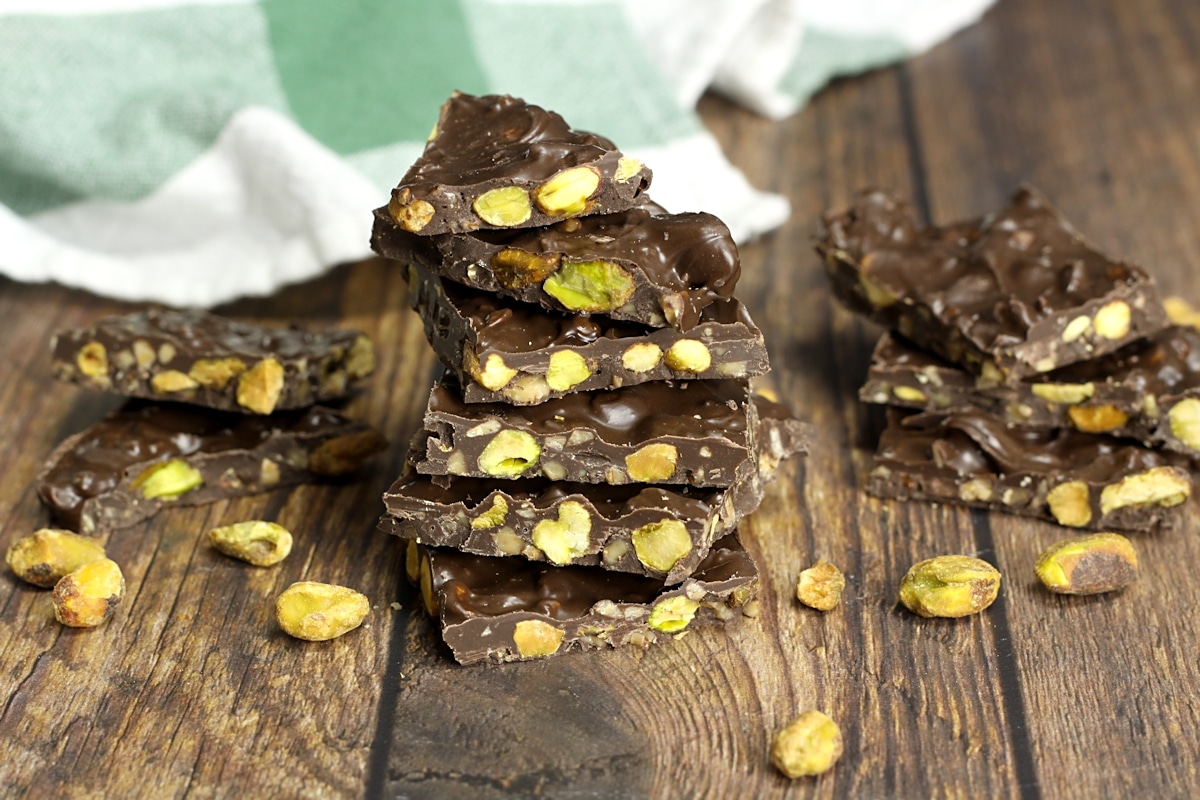 A stack of dark chocolate pistachio bark on a wooden counter top.