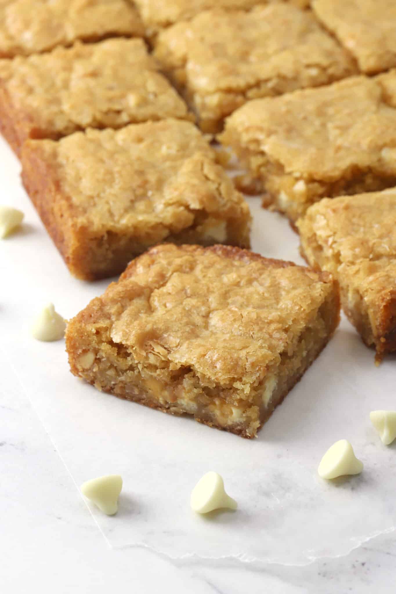 Toasted coconut blondies sliced on a piece of parchment on a counter top.