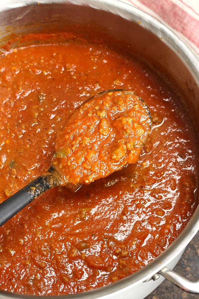 A serving spoon of spaghetti sauce in a stock pot.