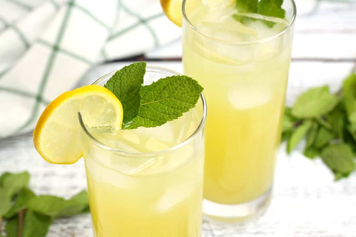 A lemon slice and mint leaf on top of a glass of lemonade.