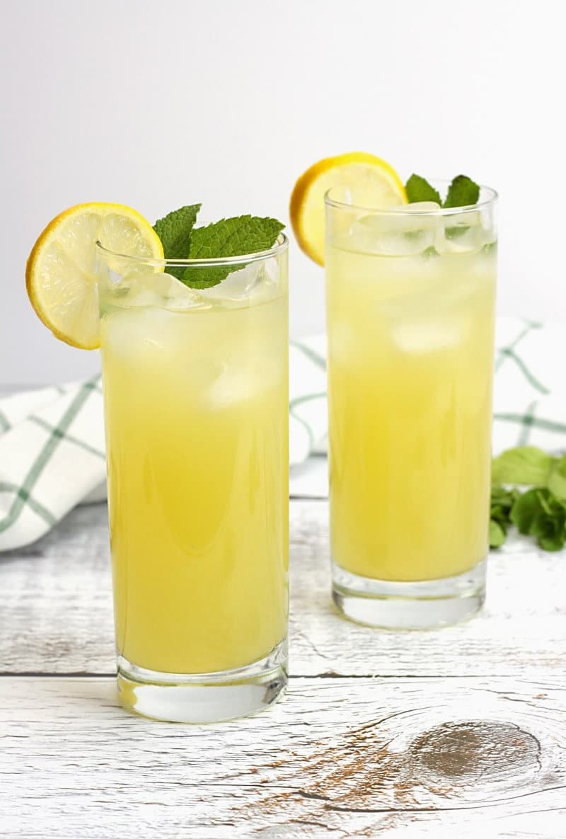 Two glasses of lemonade on a white wood counter top.