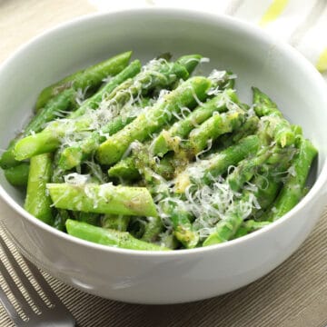 White bowl filled with blanched asparagus with parmesan cheese.