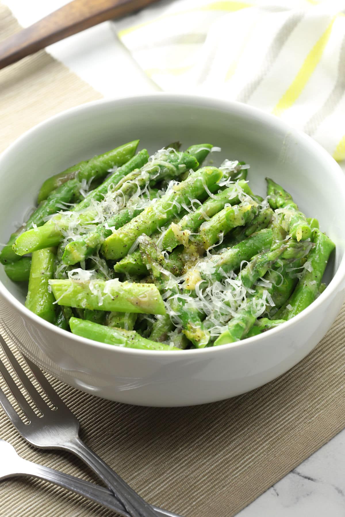 White bowl filled with blanched asparagus with parmesan cheese.