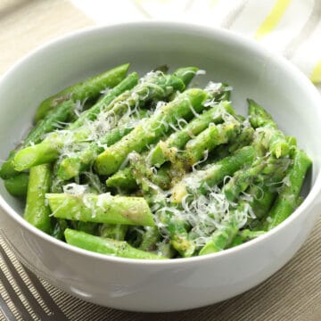 White bowl filled with blanched asparagus with parmesan cheese.