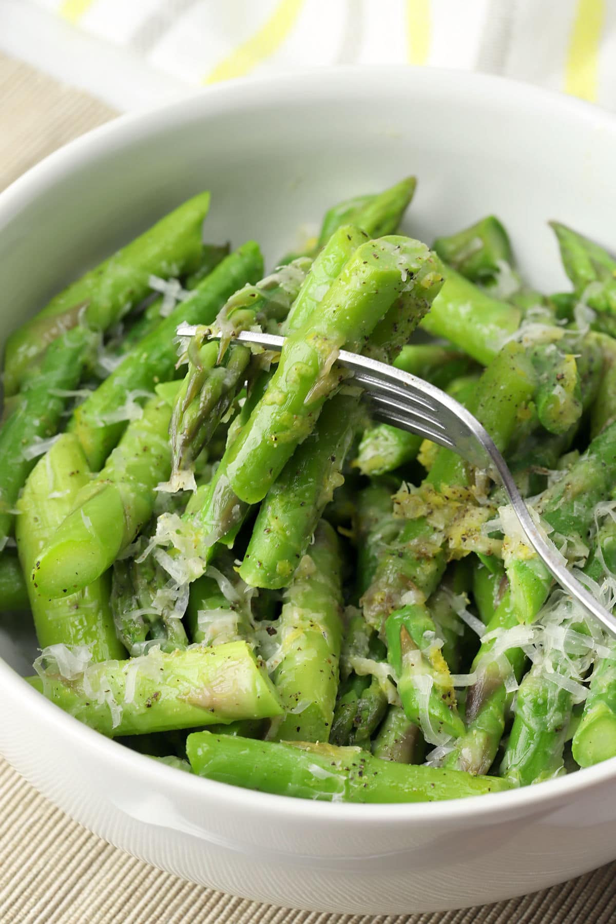 A fork filled with cooked asparagus topped with shredded parmesan and lemon zest.