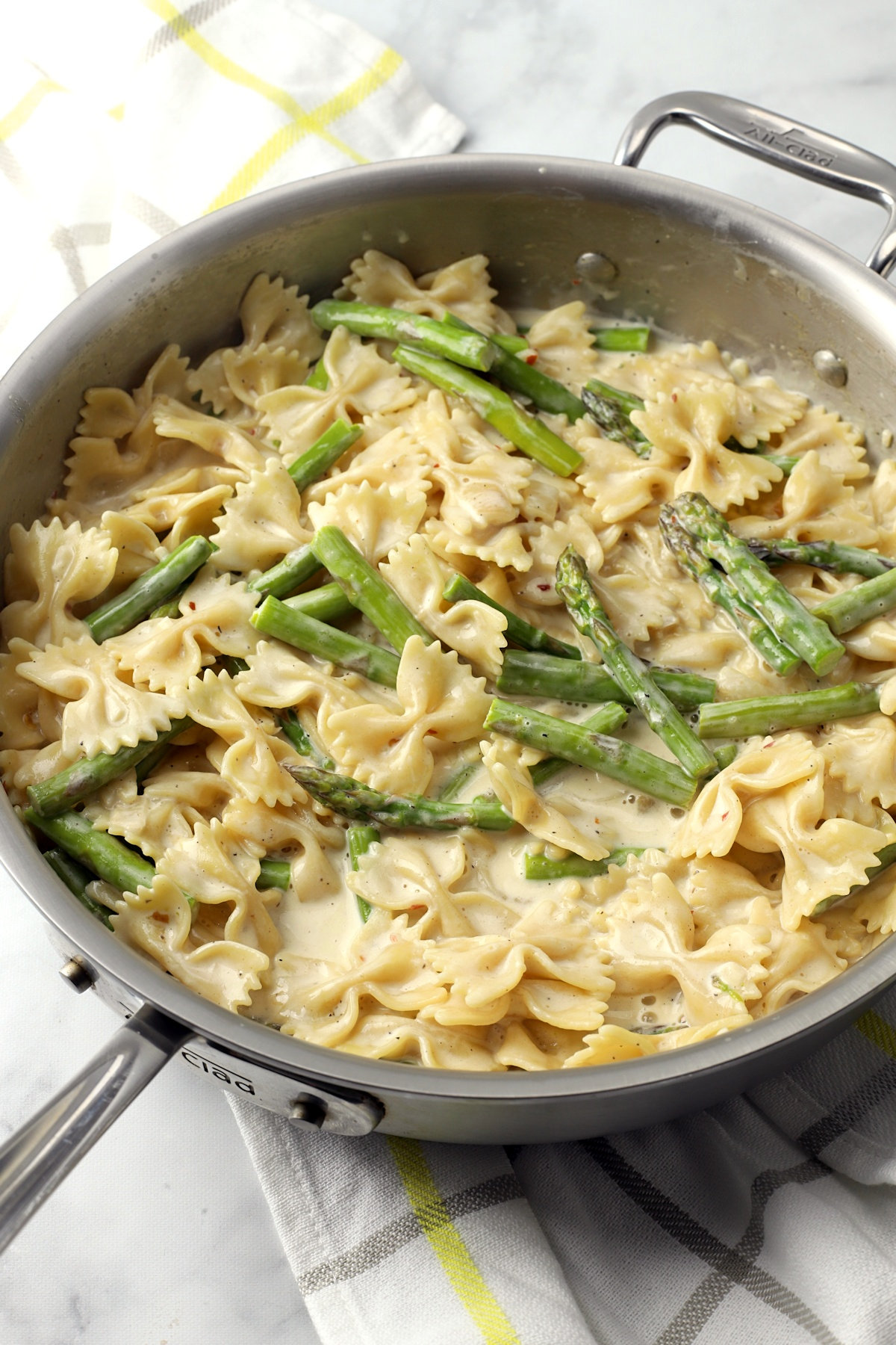 A saute pan filled with bow tie pasta and asparagus.