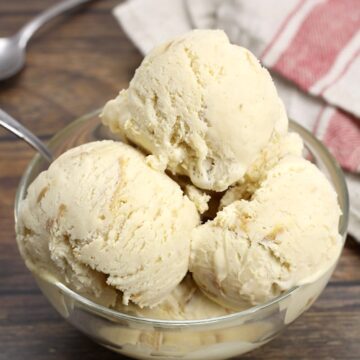 A glass bowl with three scoops of ice cream, with metal spoons.