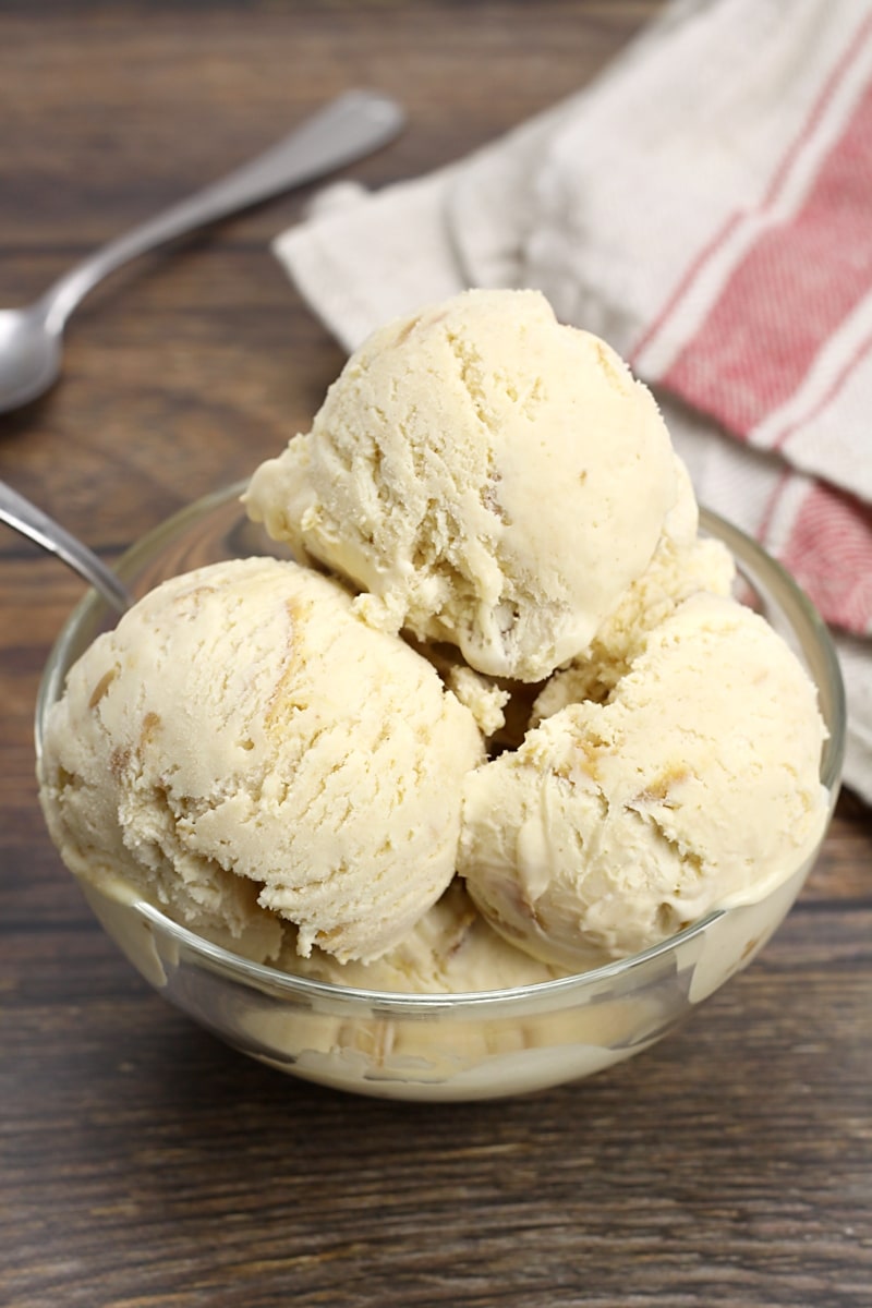 A glass bowl with three scoops of ice cream, with metal spoons.