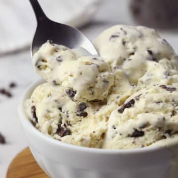 A metal spoon scooping into a bowl of mint chocolate chip ice cream.