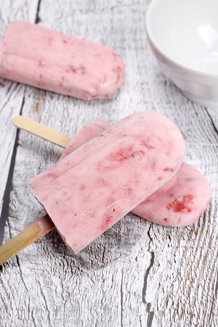 Strawberry popsicles on a white wood counter top.