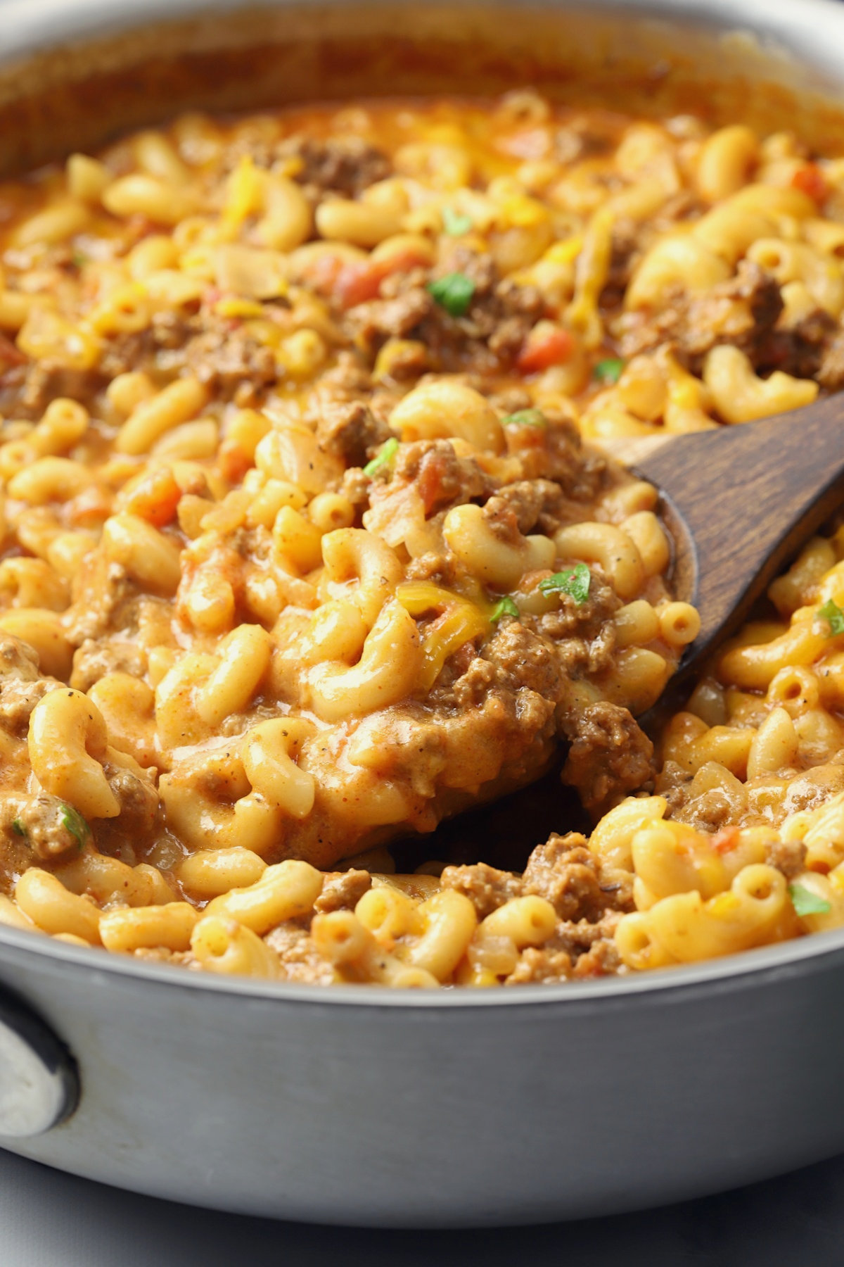 A wooden serving spoon scoops up cheesy pasta from a pan.