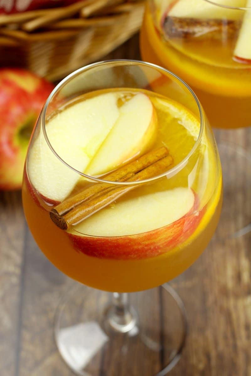 A wine glass filled with orange sangria with fruit and a cinnamon stick.