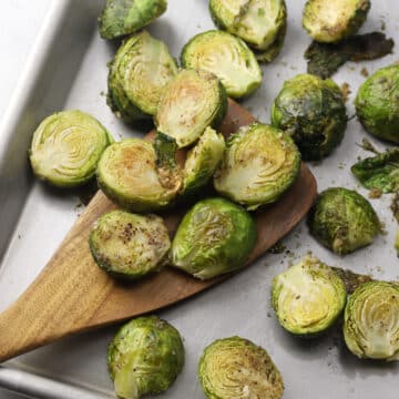 Wooden spatula scooping brussels sprouts from a sheet pan.