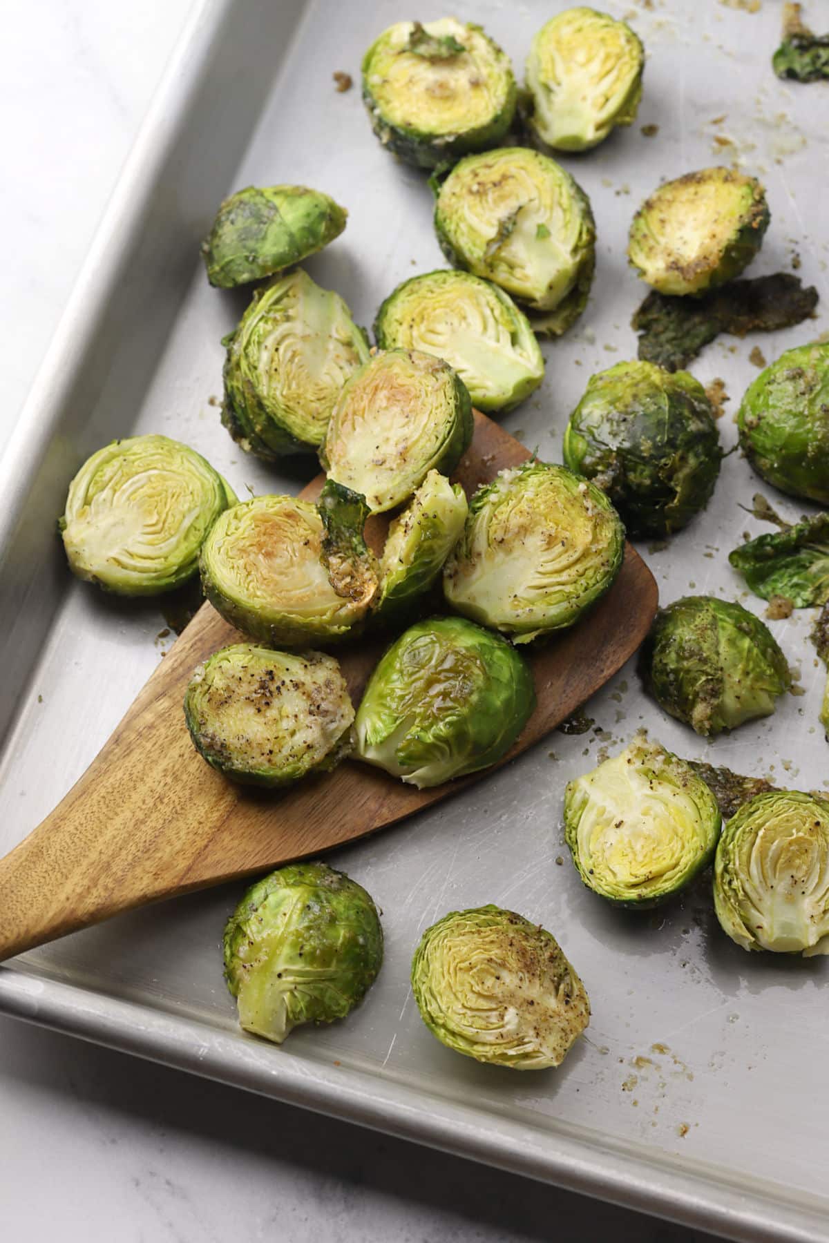 Wooden spatula scooping brussels sprouts from a sheet pan.