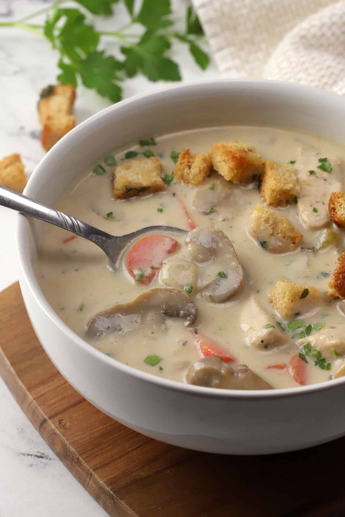 A bowl of creamy mushroom soup topped with croutons with a spoon.