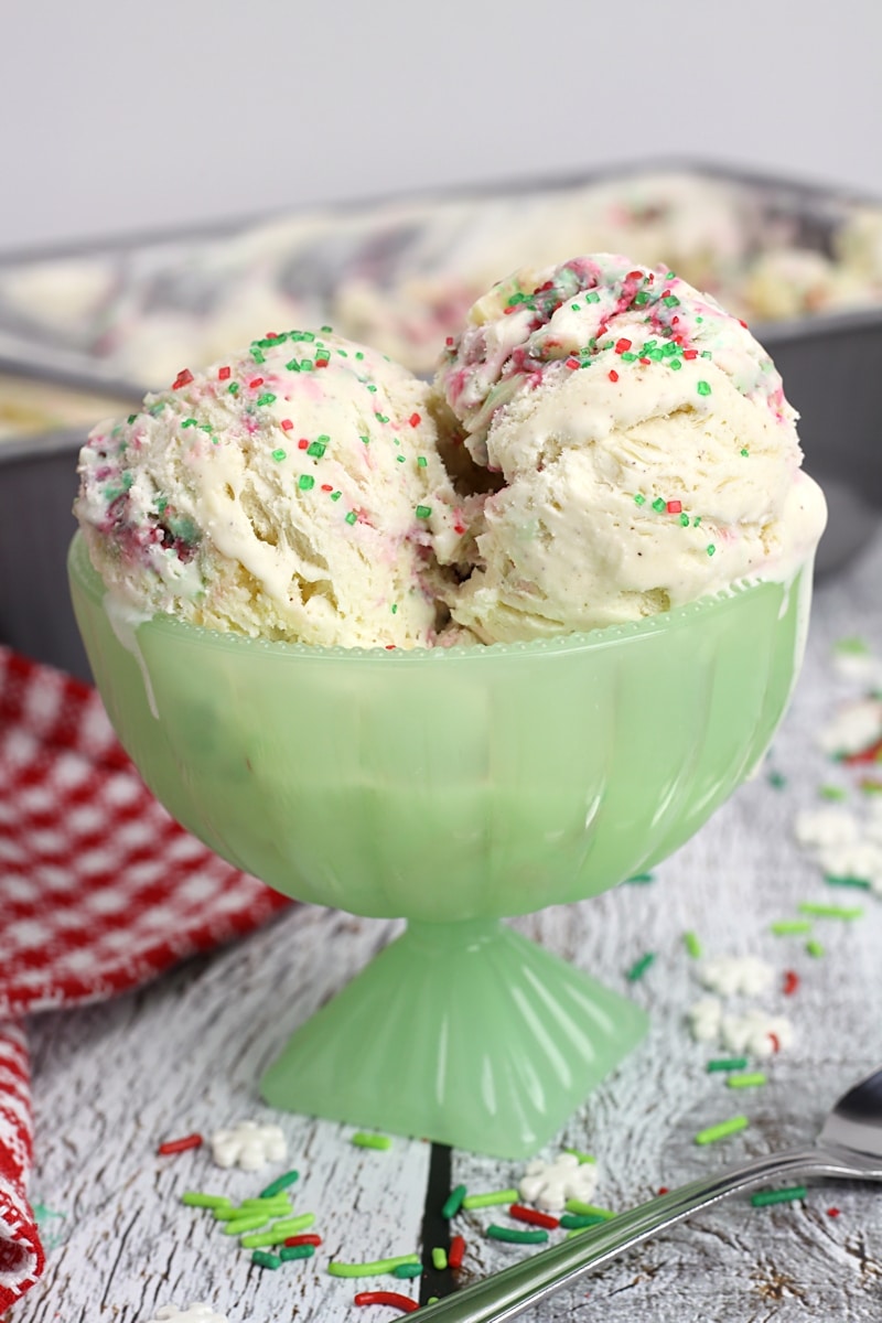 A green bowl filled with scoops of ice cream and red and green sprinkles.