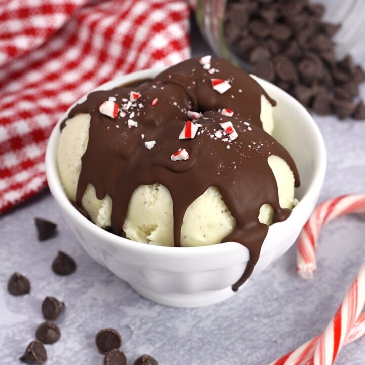 A bowl of ice cream topped with chocolate shell and candy cane crumbles.