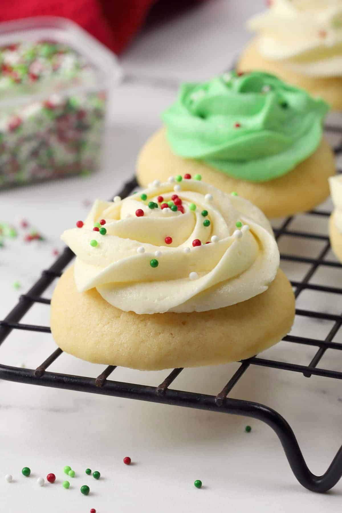 Soft frosted Christmas cookies on a black cooling rack.
