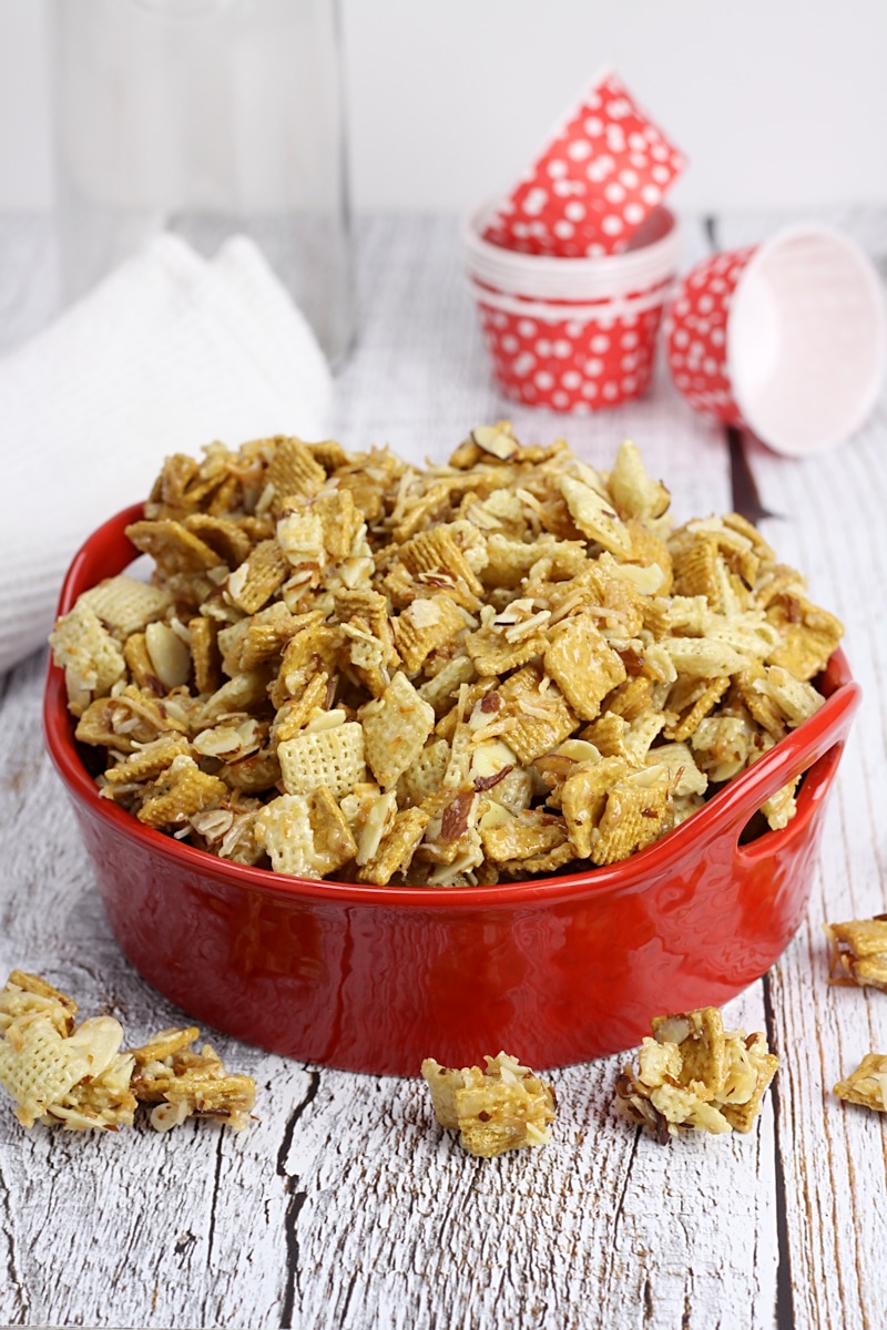 A red serving bowl filled with snack mix, with red paper cups ready to serve.