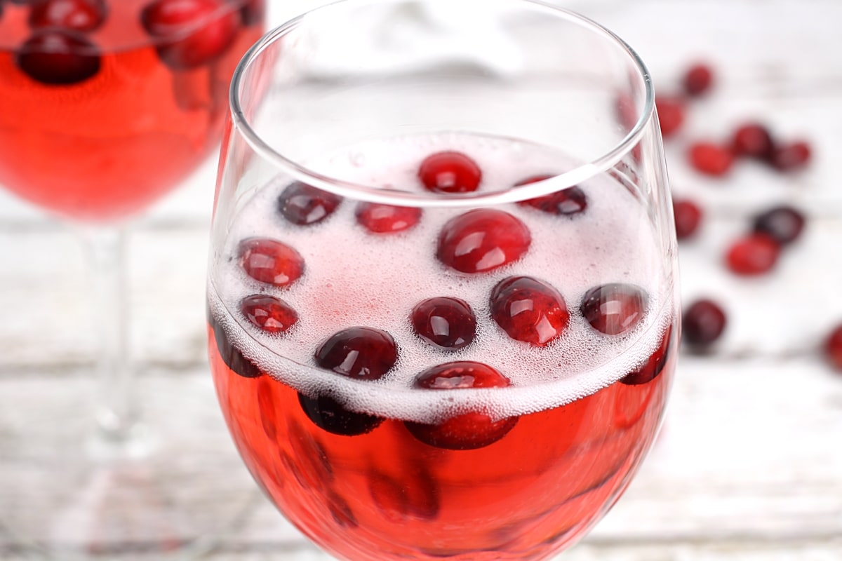 Fizzy prosecco added to a wine glass with cranberries.