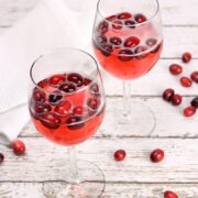 Two wine glasses filled with red wine and cranberries.